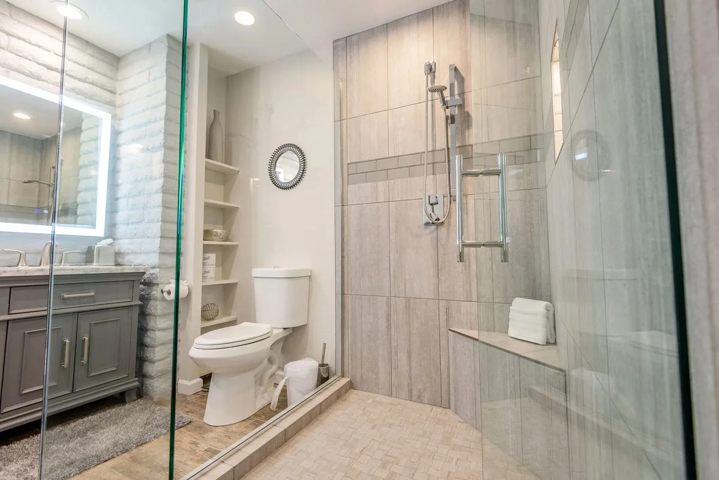 Sedona primary bath after: double vanity with gray cabinets, marble top, backlit mirrors and whitewashed brick accent wall